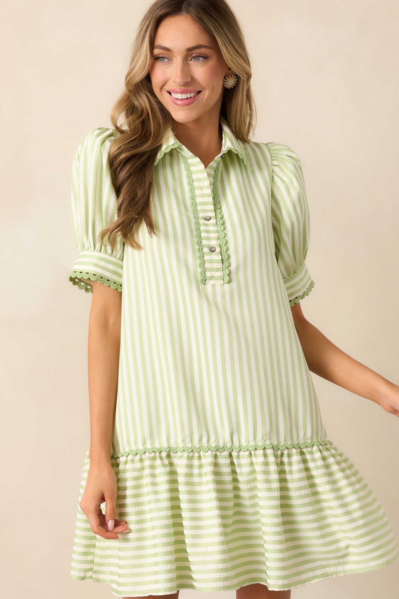 A close-up of the collared neckline and functional buttons, showcasing the ric rac trim along the collar and the soft green hue.