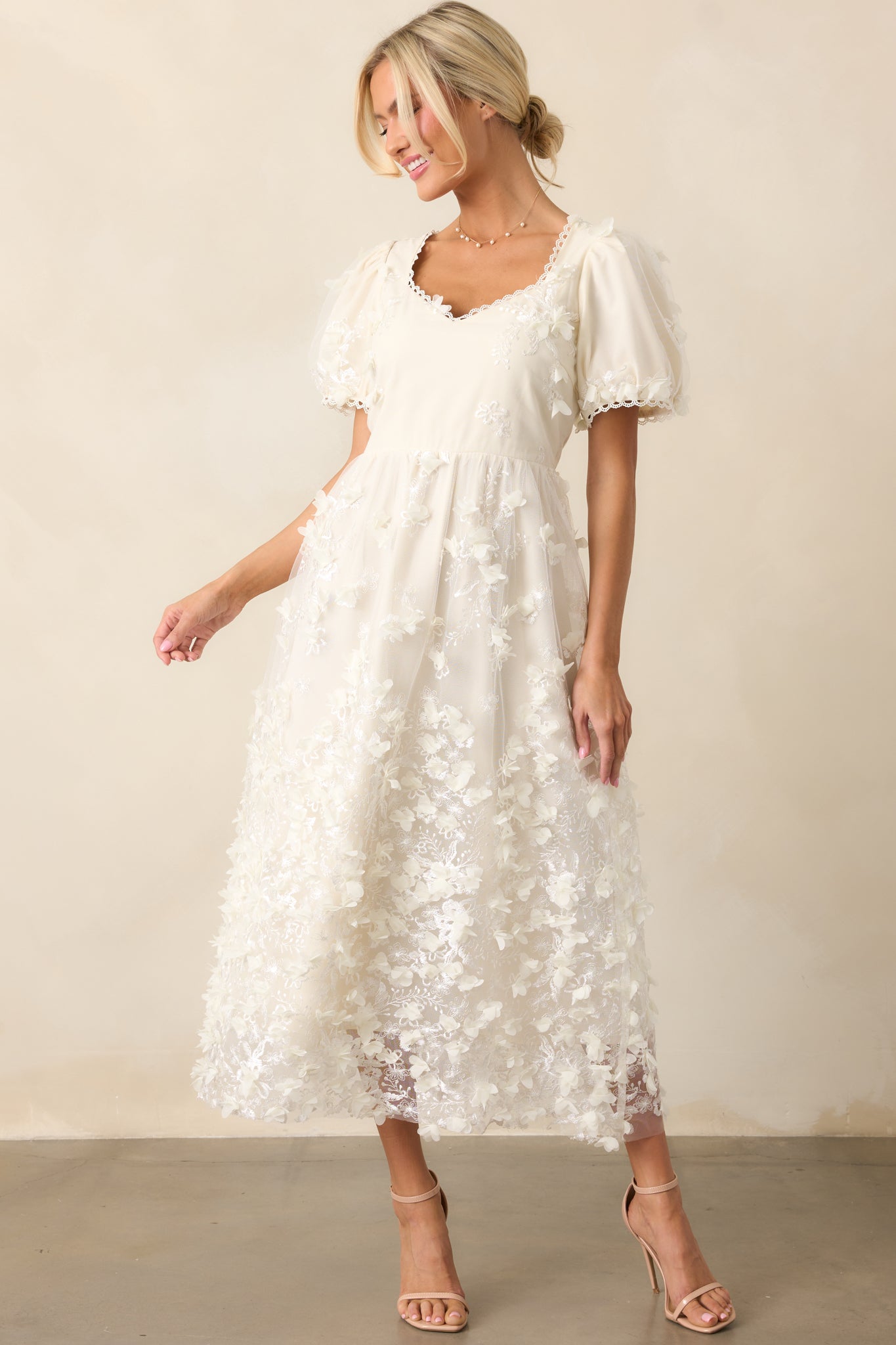 An ivory midi dress with a rounded neckline, floral applique overlay, and short puff sleeves, displayed from the front. The delicate texture of the applique adds depth to the design.