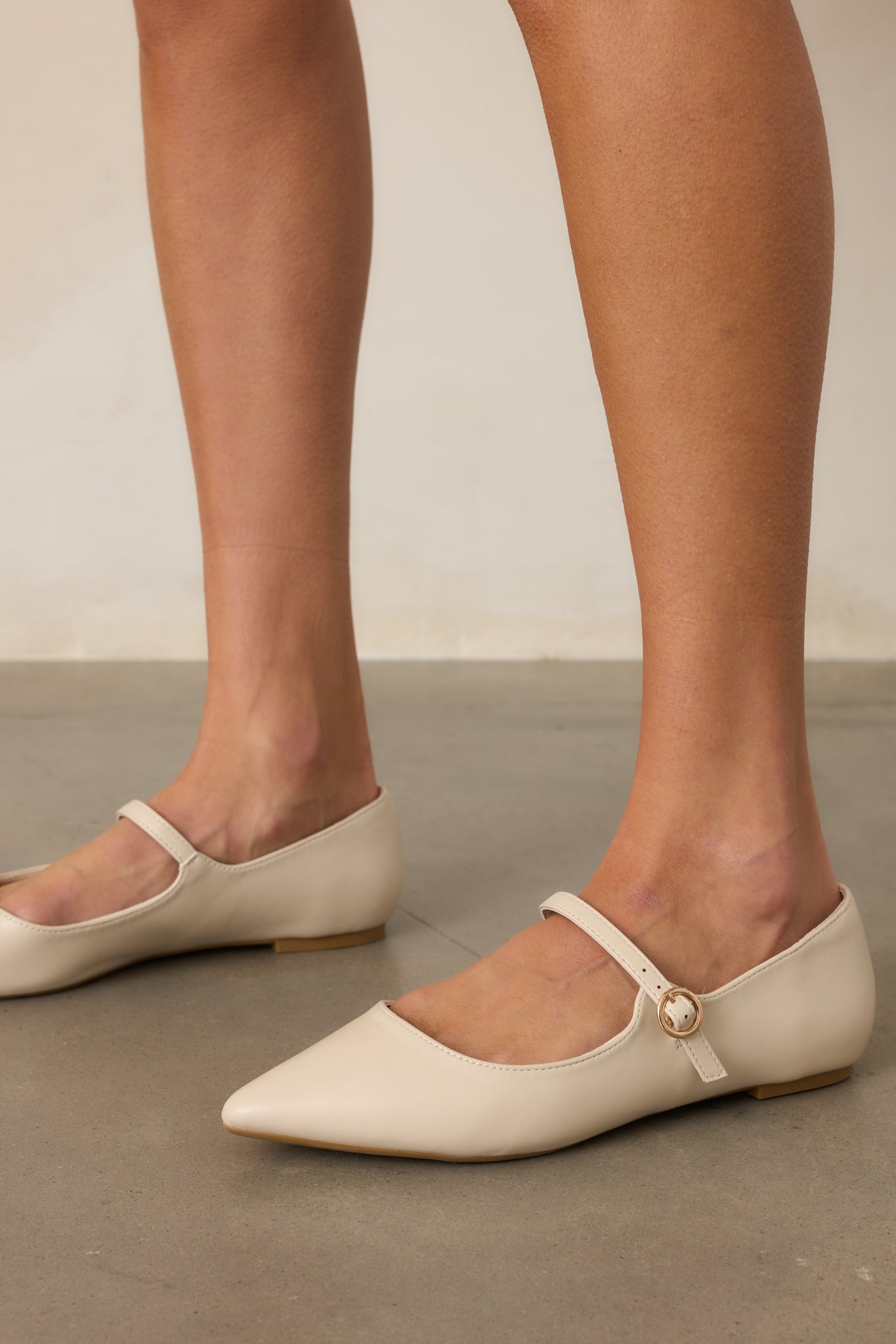 Ivory flats with a pointed toe, featuring a sleek material and a decorative buckle across the foot strap.