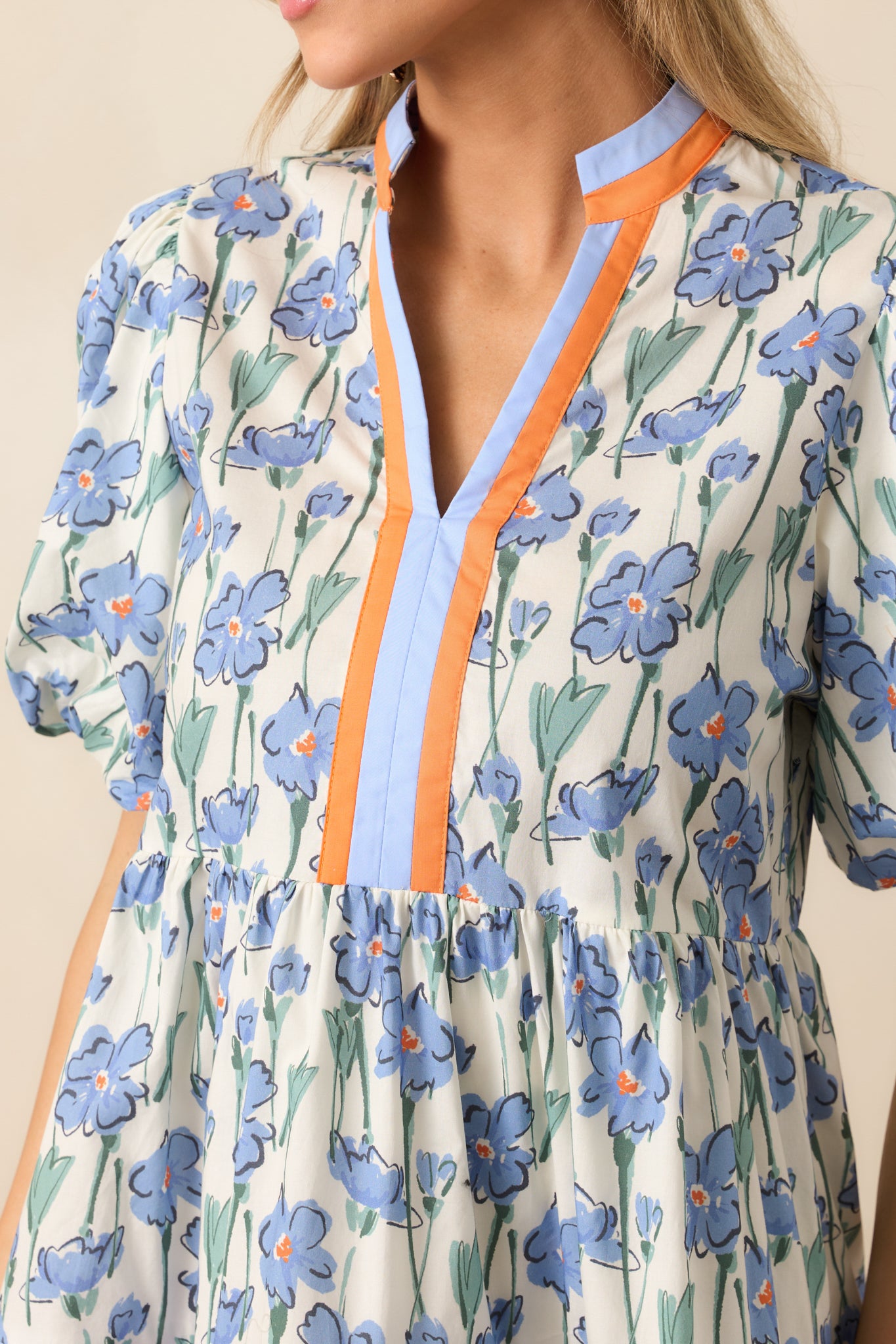 A close-up of the v-neck neckline, short puff sleeves, and the tiered skirt with orange and blue striped hems, showcasing the dress’s charming design.