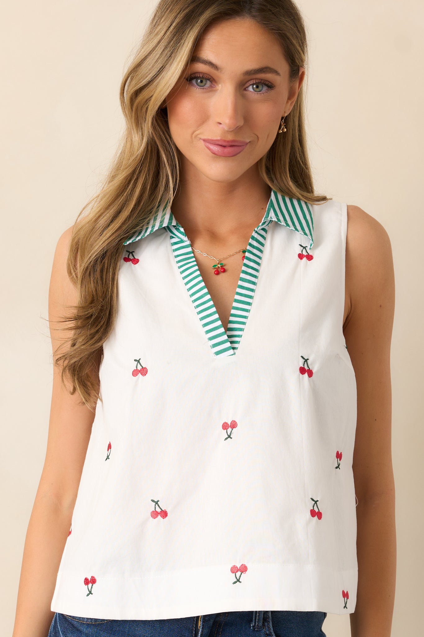 A breezy ivory blouse with embroidered cherry icons, a green and white striped collar, and a relaxed sleeveless silhouette.