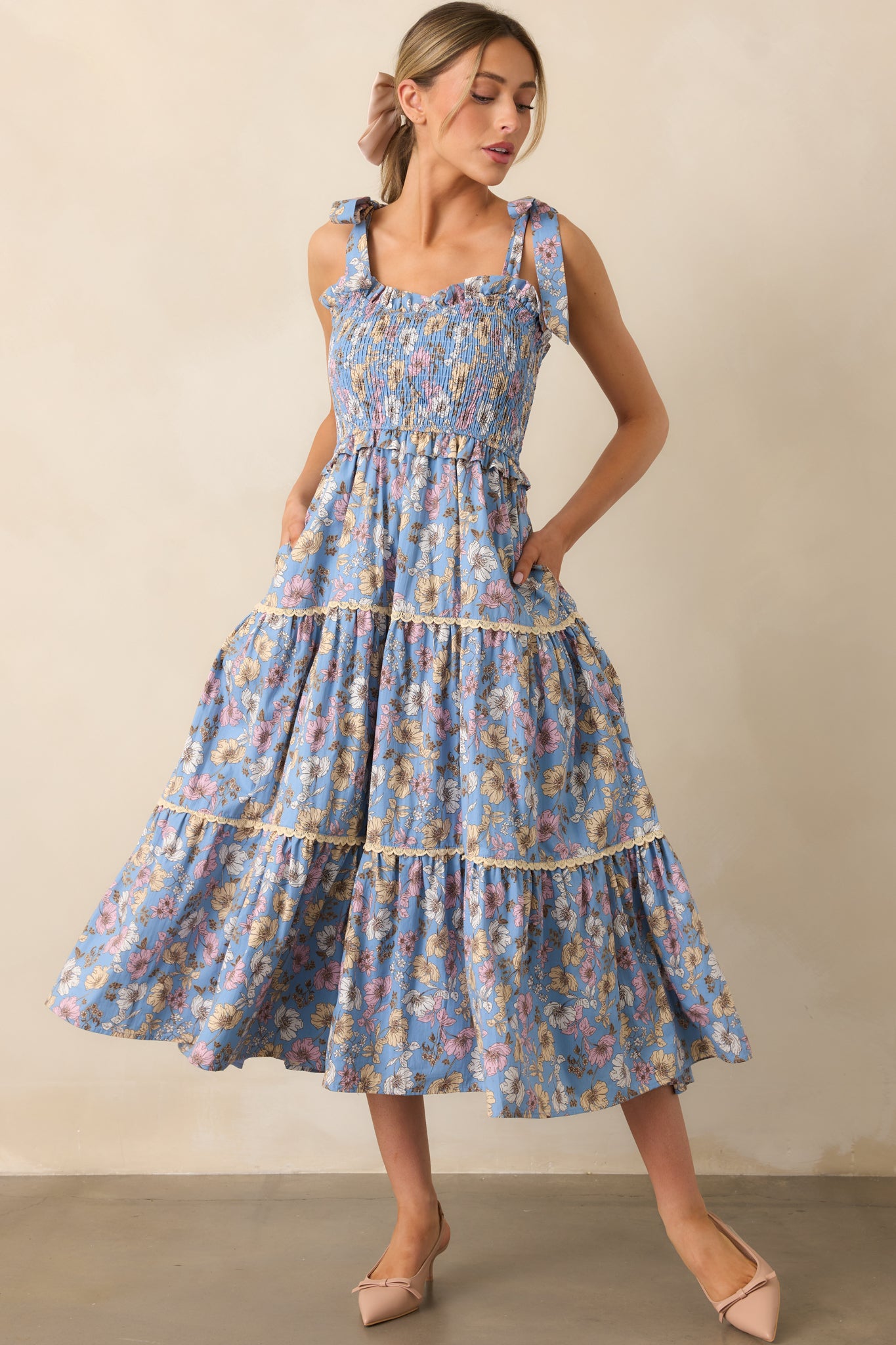 An ash blue dress featuring a sweetheart neckline, a soft floral print, and adjustable self-tie bow straps, with a lace tiered skirt adding texture and charm.

