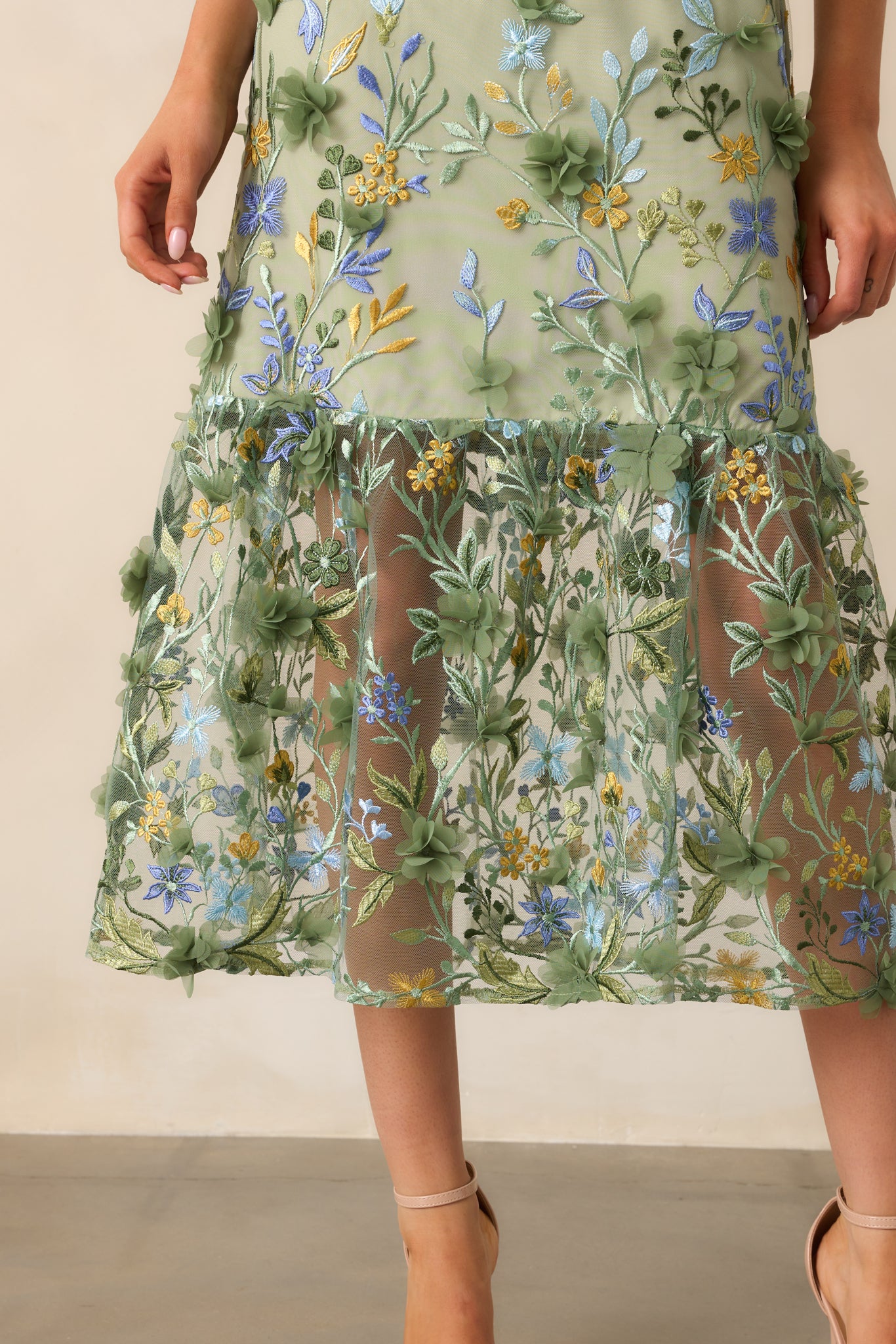 A close-up of the floral embroidered overlay at the hemline of the green midi dress, showcasing the intricate stitching and delicate details that enhance the soft, flowing effect of the dress.