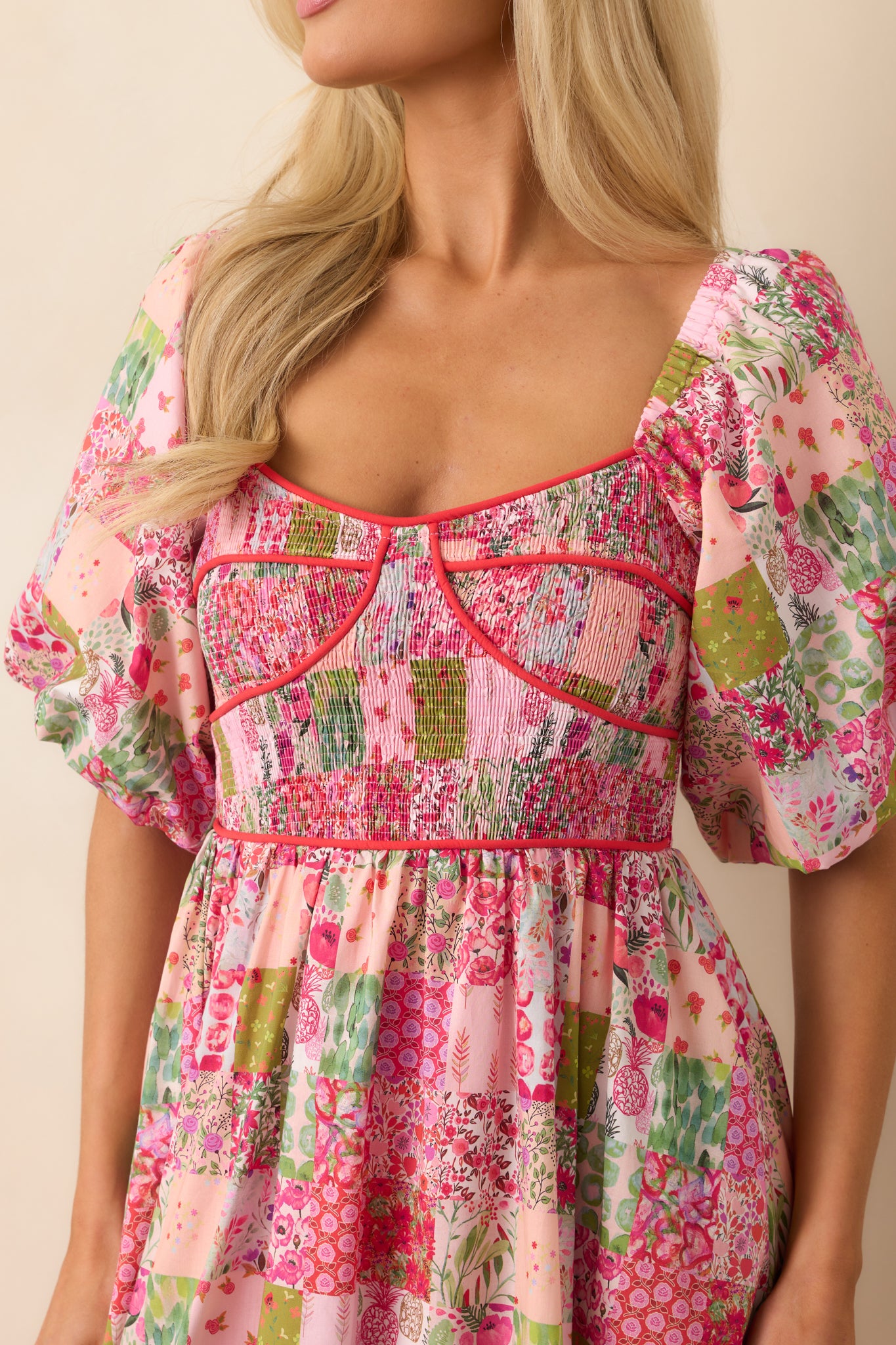 A close-up of the pink midi dress highlighting the textured smocked bodice, delicate puff sleeves, and intricate patchwork print.