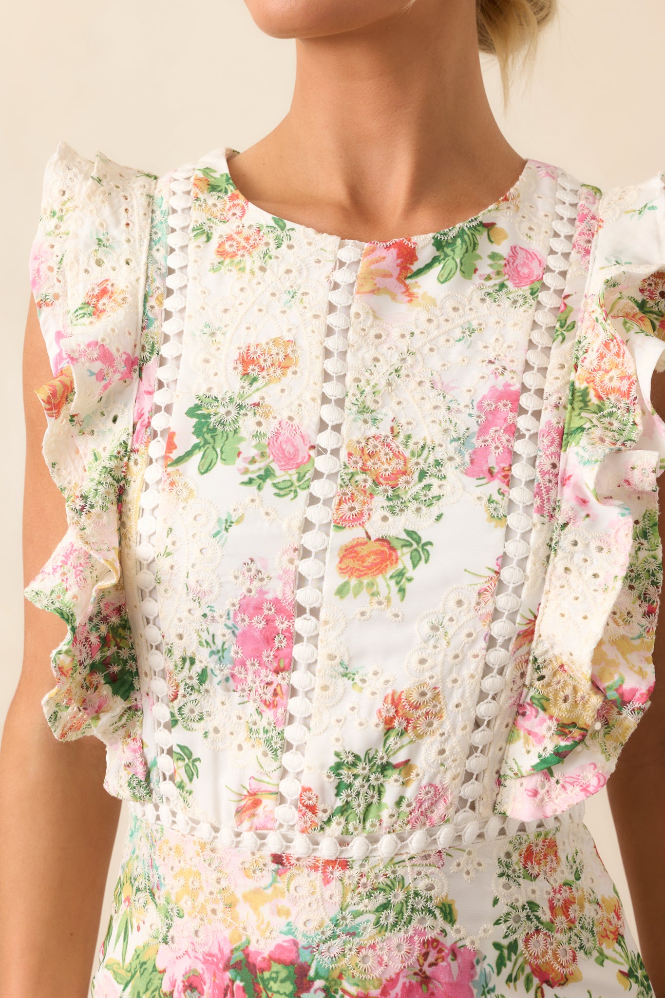 Focused on the elegant eyelet embroidery scattered throughout the ivory mini dress, adding texture and sophistication to the floral pattern.