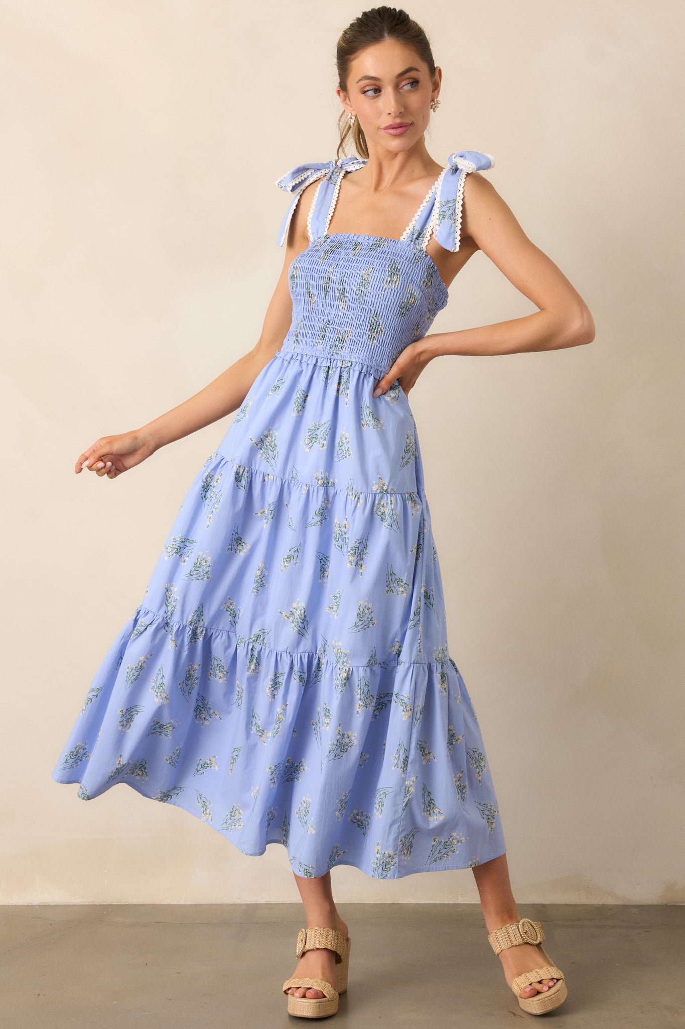 A periwinkle dress with a fully smocked bust, square neckline, and tiered skirt, complete with delicate ruffle details and functional pockets.