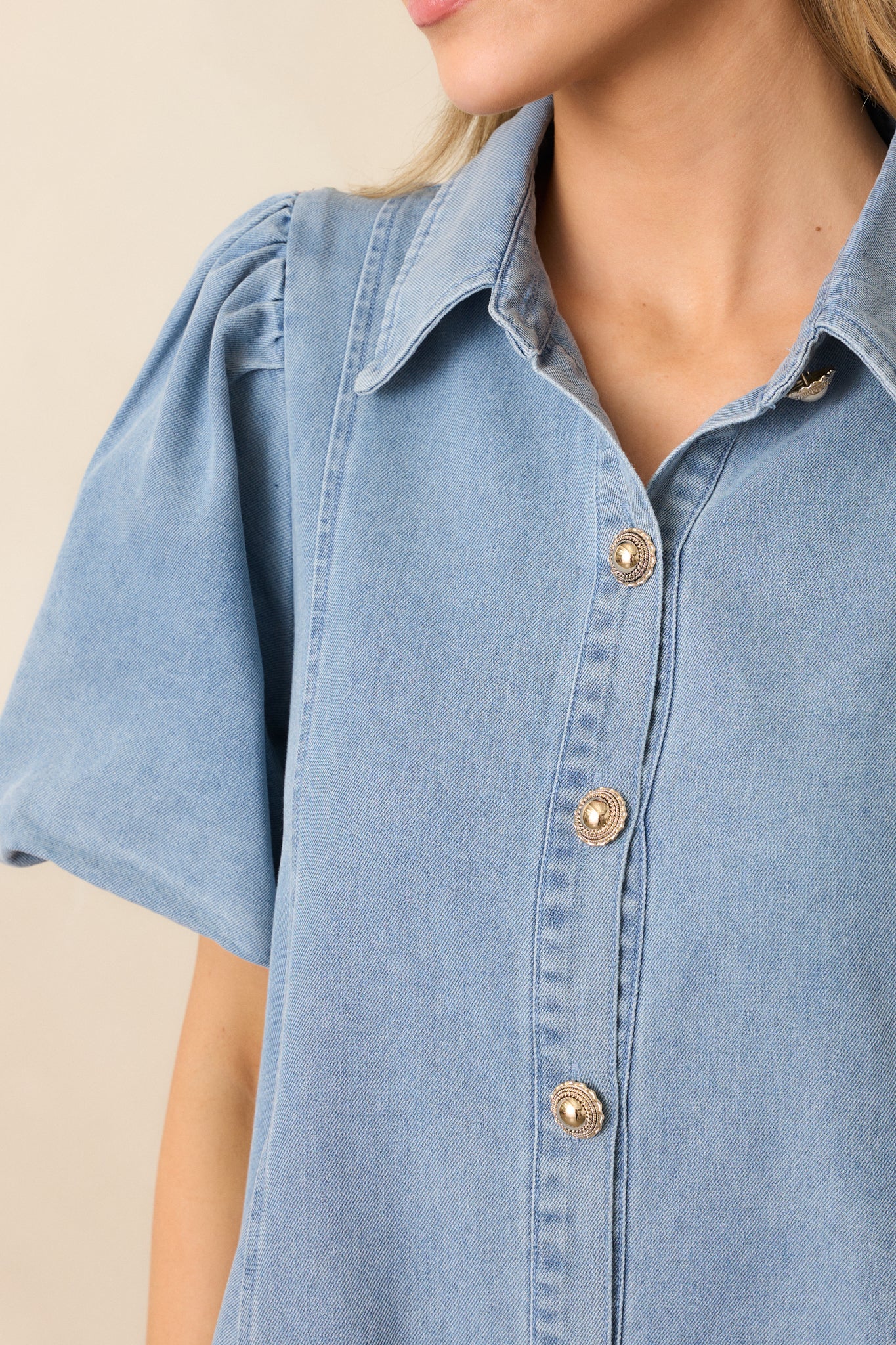 A close-up of the gold button front and collared neckline, showcasing the denim fabric and detailed stitching of this mini dress.