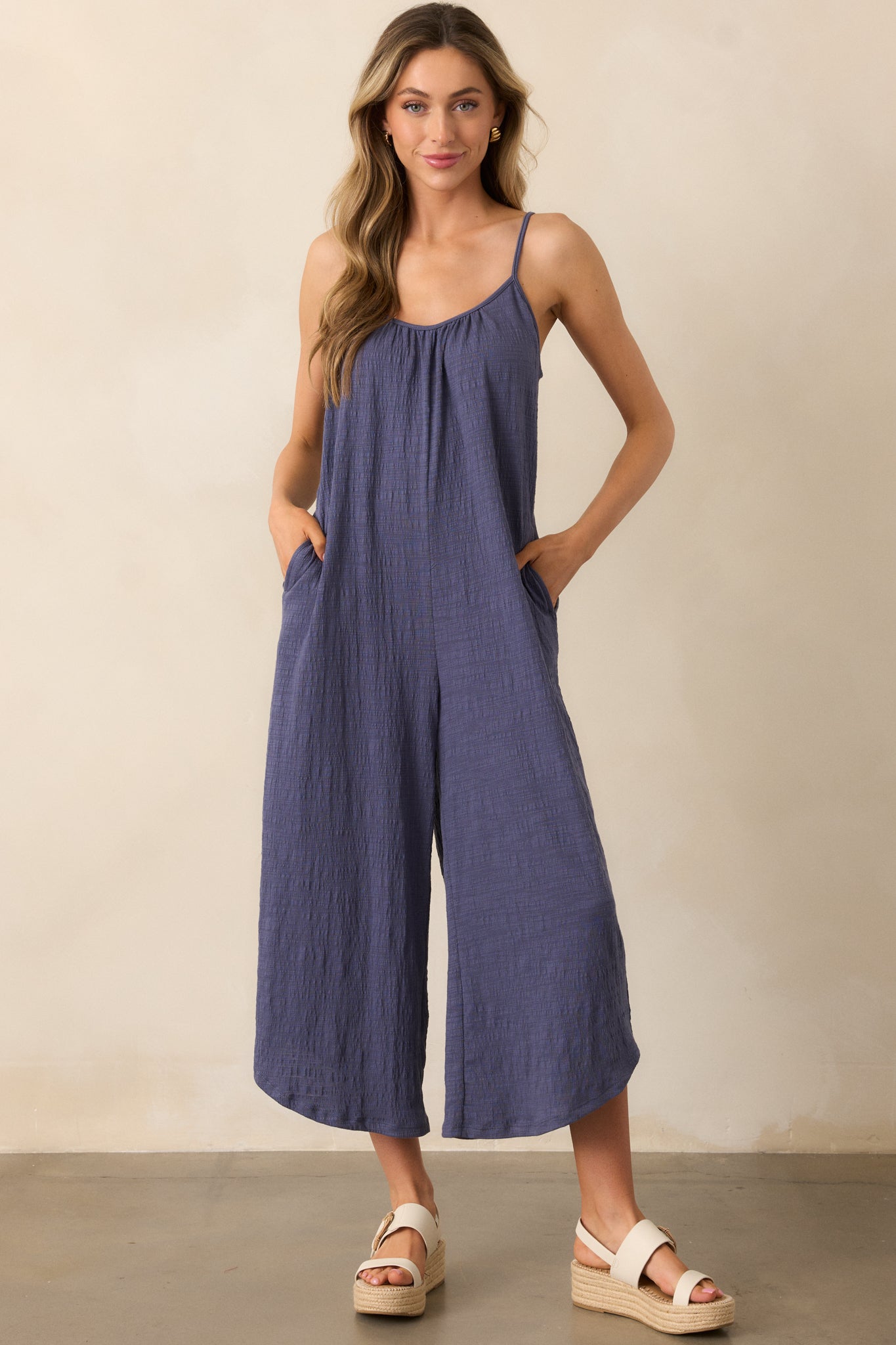 This textured slub fabric jumpsuit in worn blue flows effortlessly, complete with adjustable spaghetti straps for a custom fit.