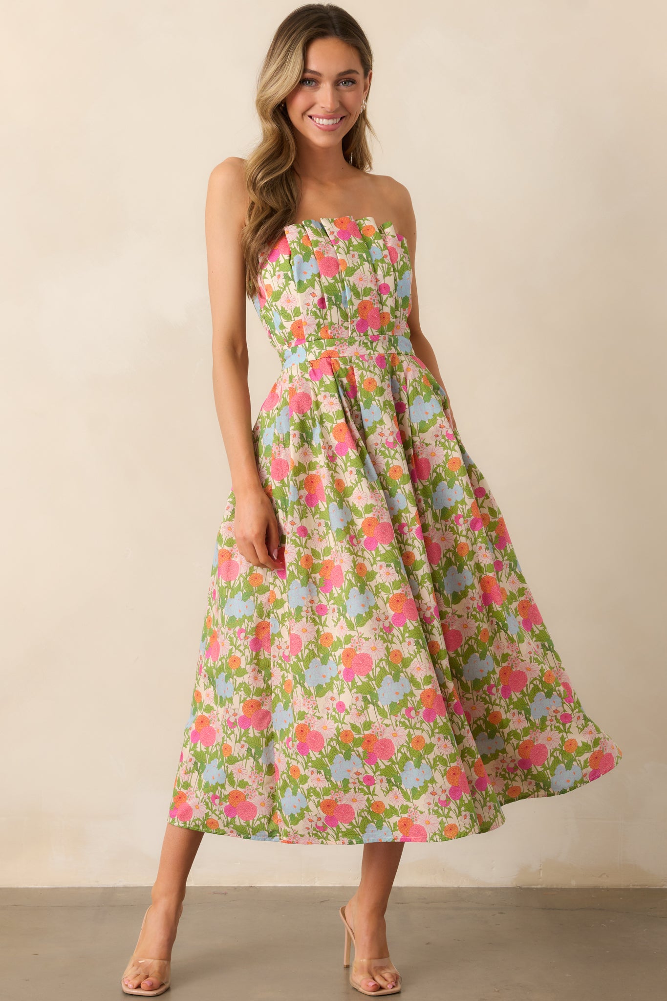  A green dress with a vibrant multicolor floral print, featuring a pleated bodice, pleated skirt, and functional hip pockets for a chic, structured look.
