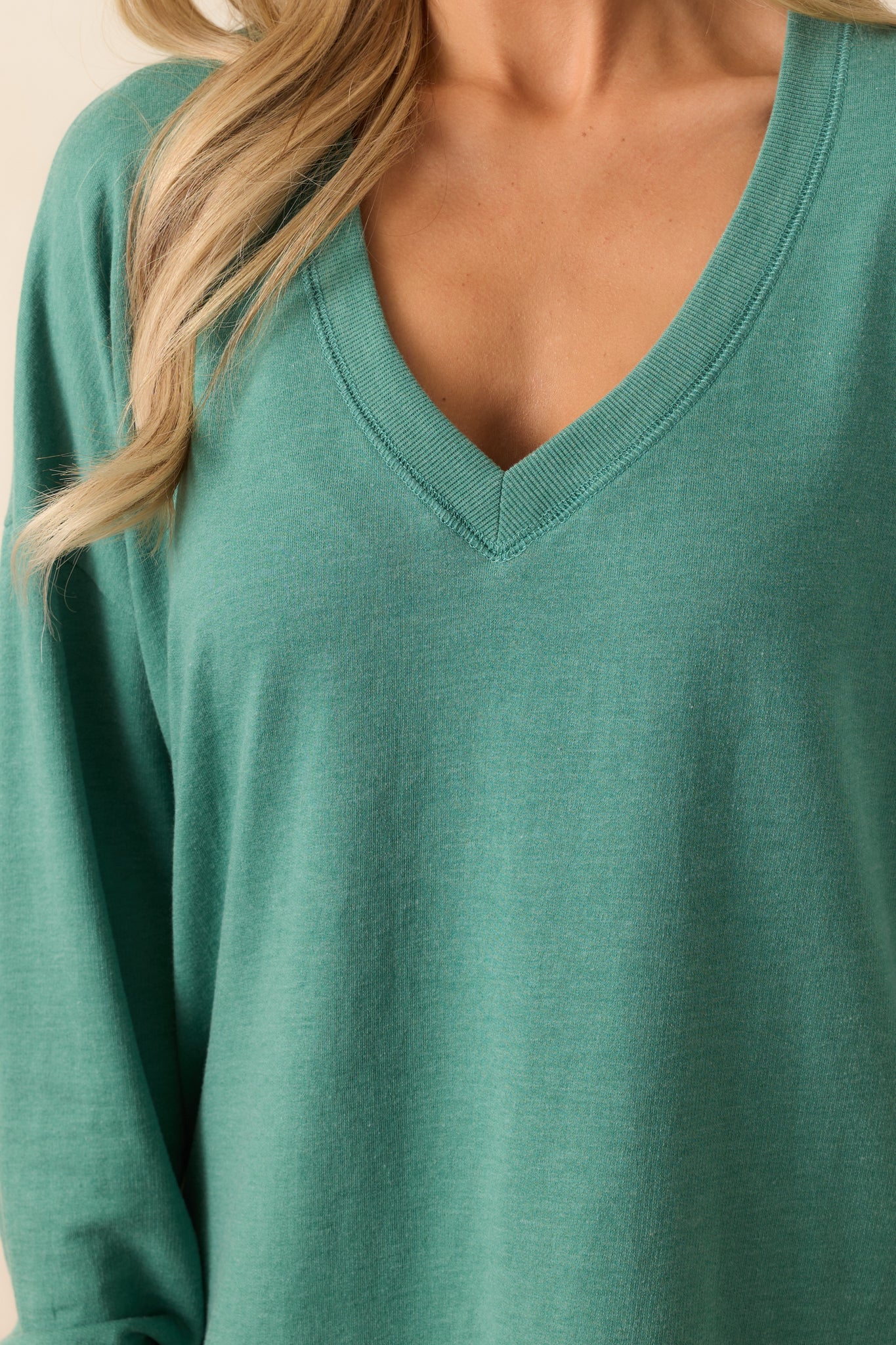 A detailed view of the fabric, showcasing the ribbed hems and v-neckline that complete the relaxed, oversized silhouette of the botanical green sweatshirt.