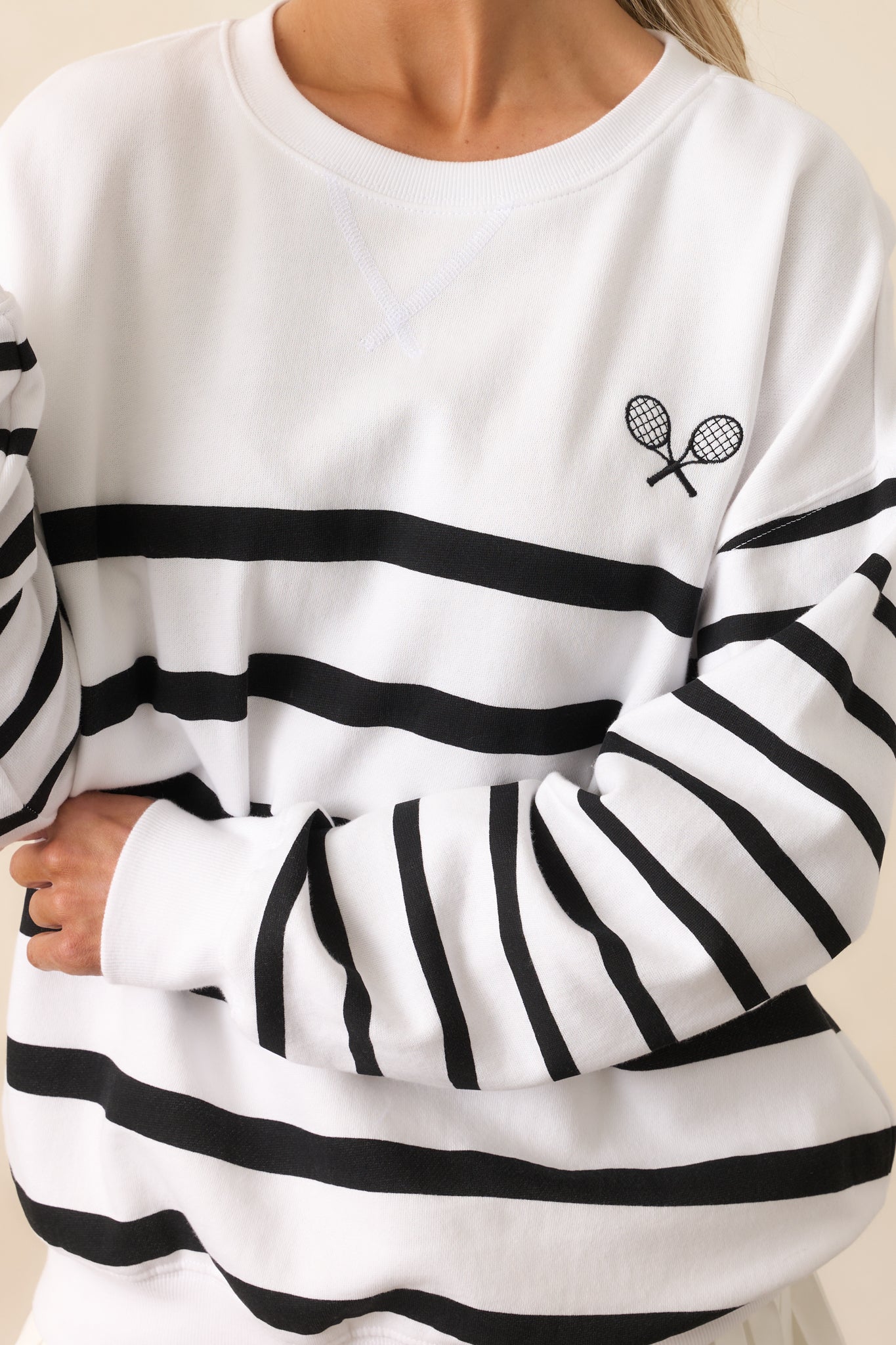 A zoomed-in look at the small tennis racquet embroidered icon, showcasing the textured stripes and ribbed hemlines that complete the top’s sporty aesthetic.