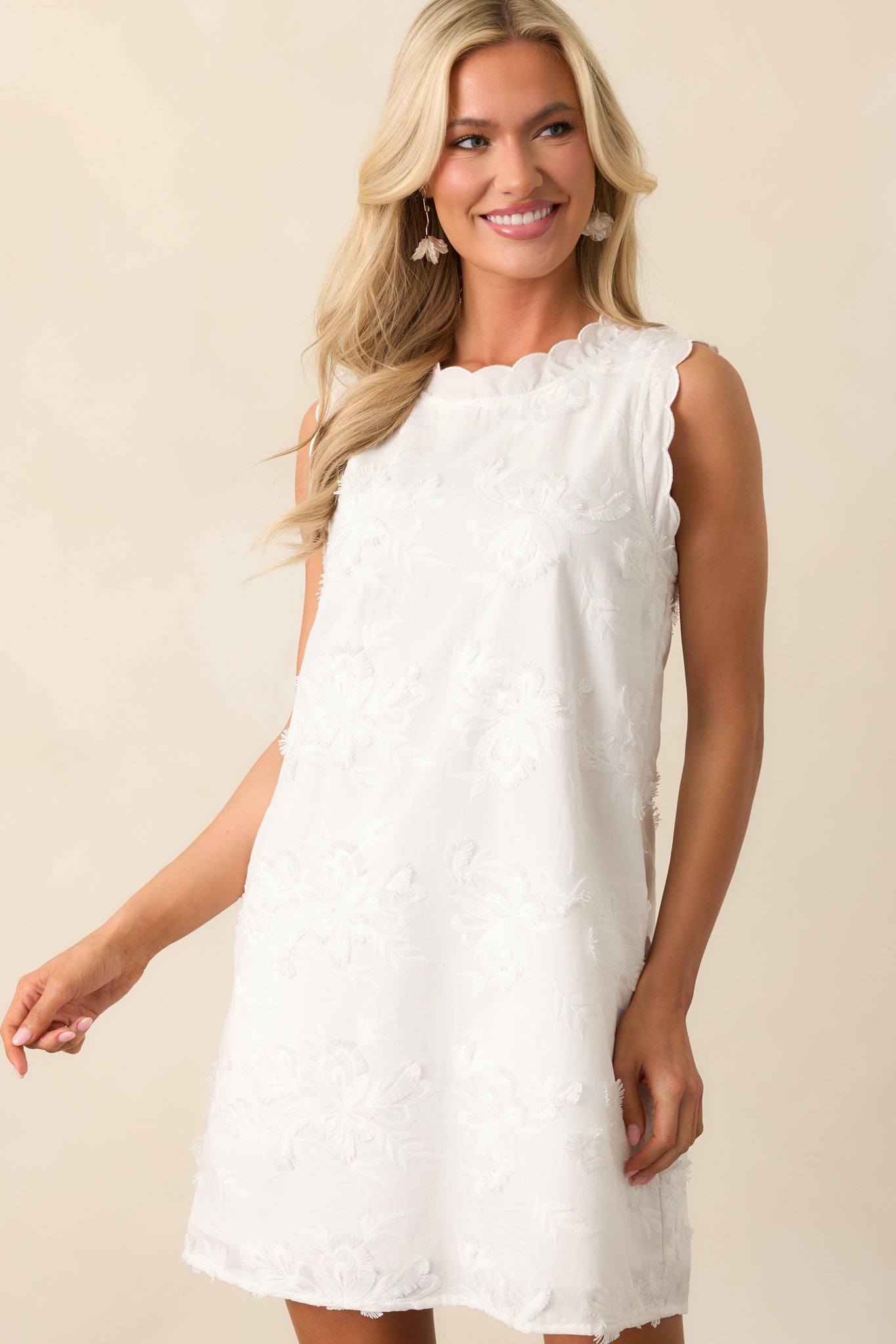 This ivory dress features a scalloped round neckline and sleeveless cut, adding a touch of elegance to the embroidered fabric.