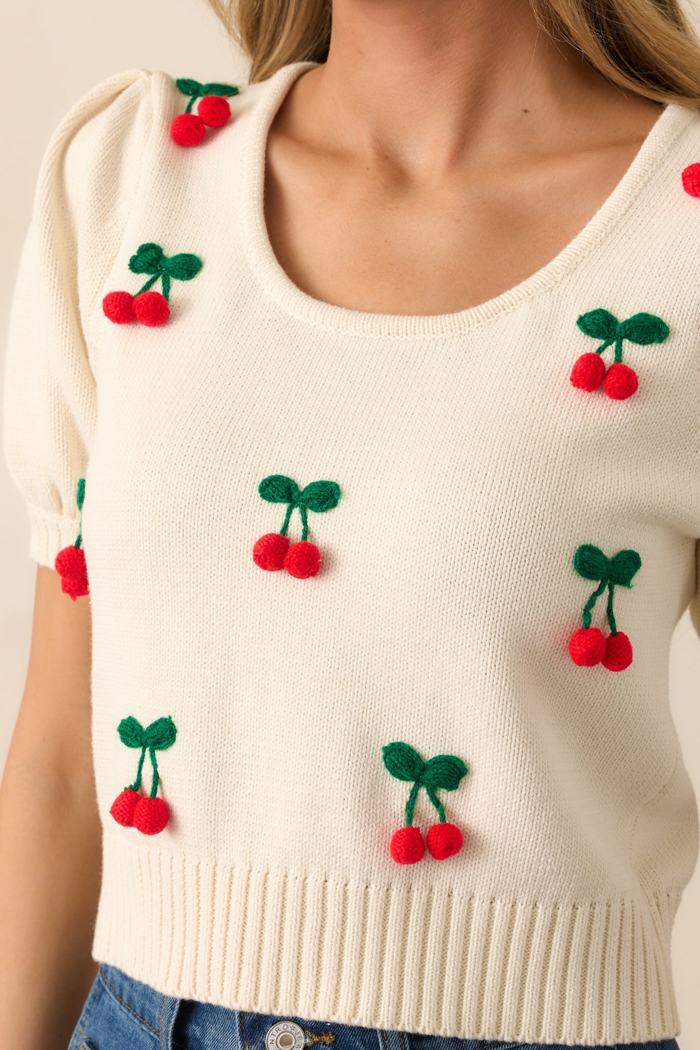 A detailed view of the 3D cherry embroidered appliqués, highlighting their texture and playful design, set against the smooth ivory knit fabric.
