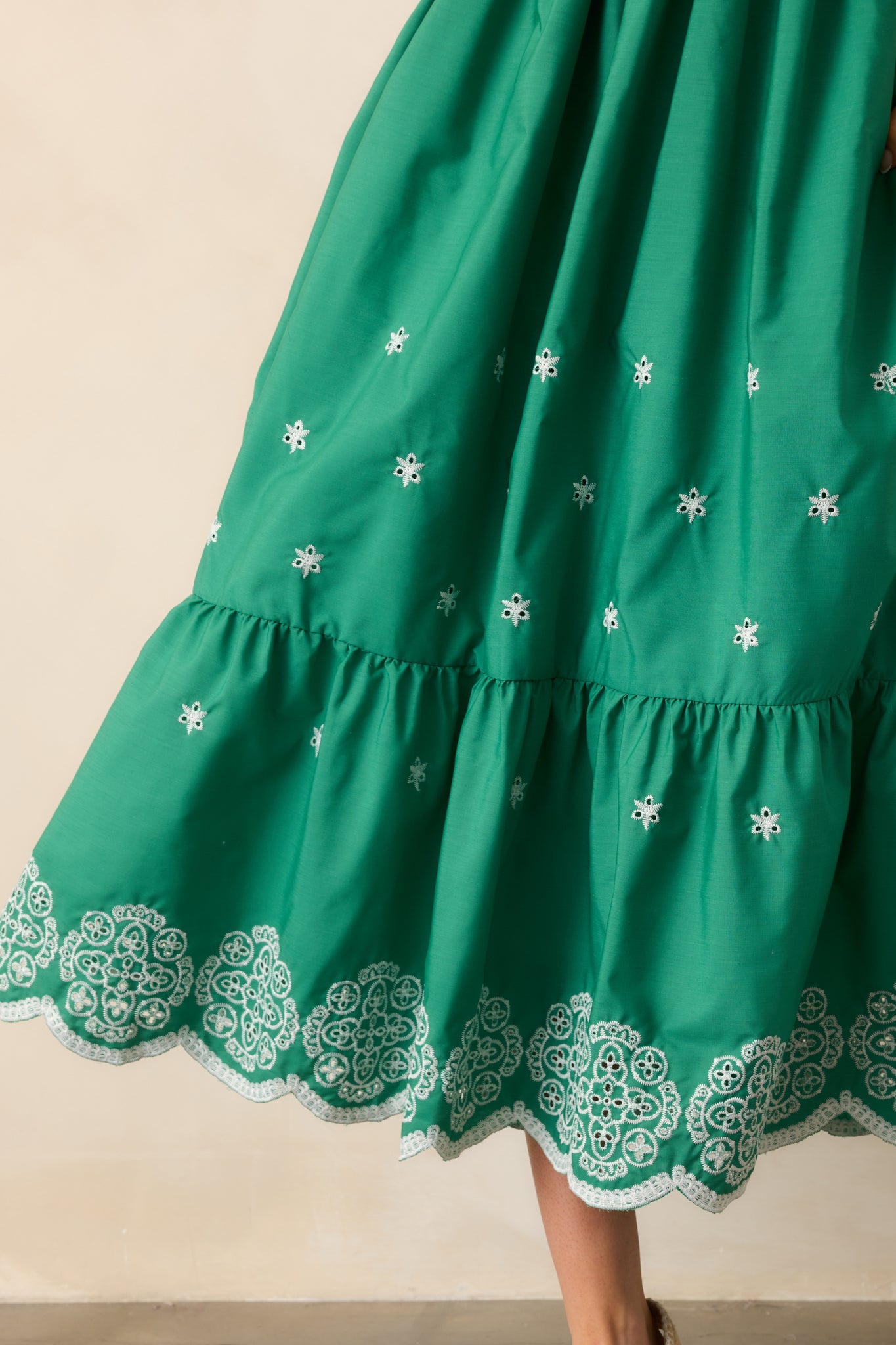 A detailed view of the embroidered eyelet detailing and tiered skirt, highlighting the intricate design and texture of the green midi dress.

