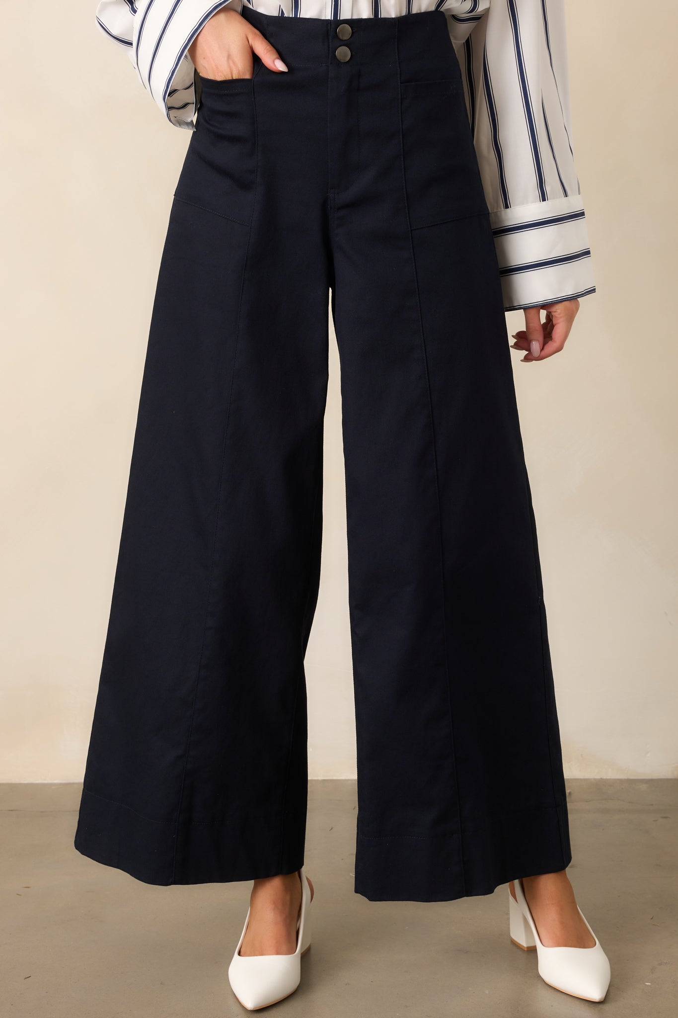 A close-up of the high-waisted design and button zipper closure of the navy pants.