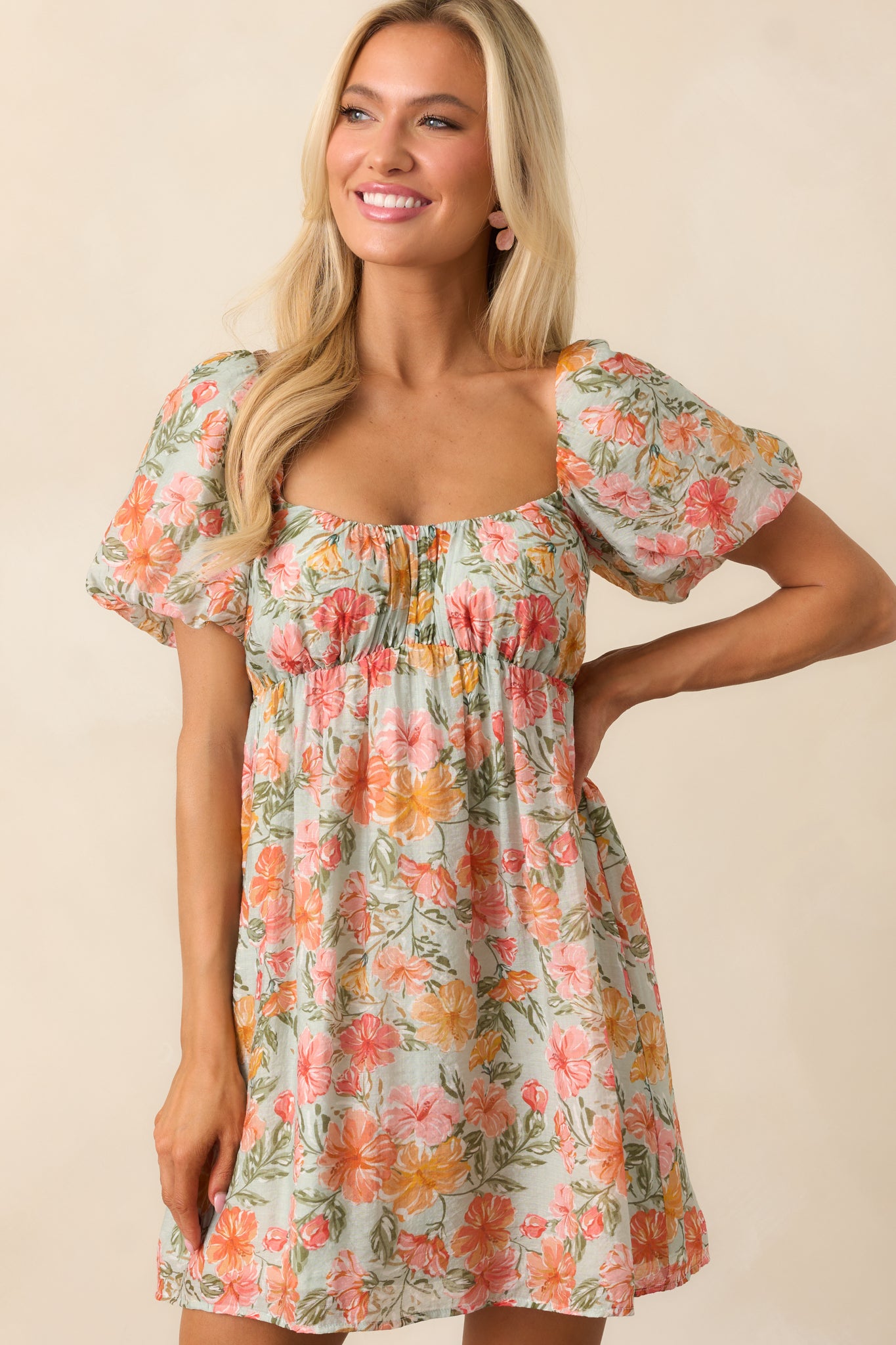 A vibrant coral mini dress with a hibiscus floral print, scoop neckline, and puff sleeves, finished with a self-tie back closure for an adjustable fit.