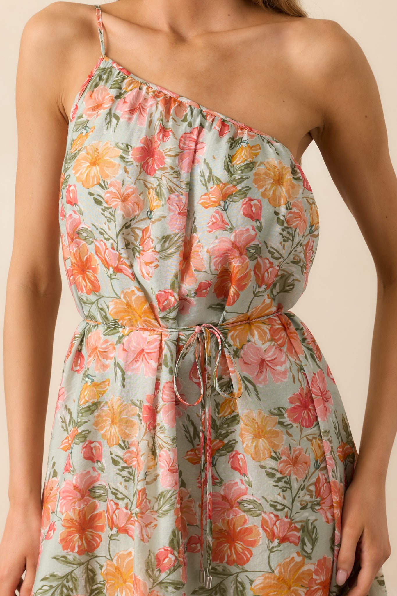 A close-up of the coral maxi dress’s one-shoulder neckline with adjustable strap and self-tie belt, emphasizing the elegant design and fine details.