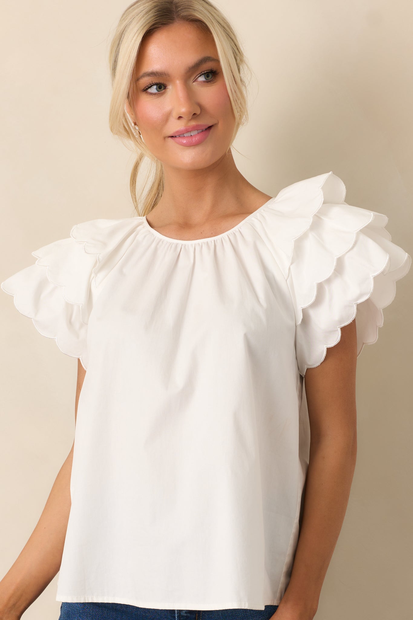 The round neckline and scalloped edges of this white top add a charming touch to its simple yet elegant design.