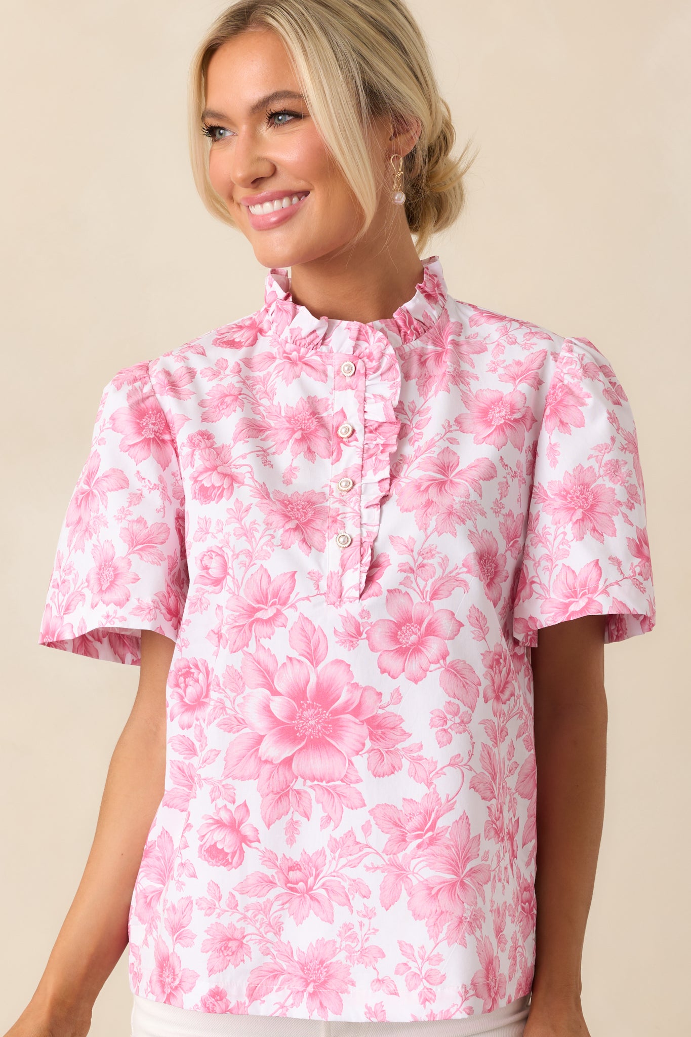 A closer look at the high ruffle neckline and ivory faux pearl buttons of the pink top, highlighting its soft, feminine details.