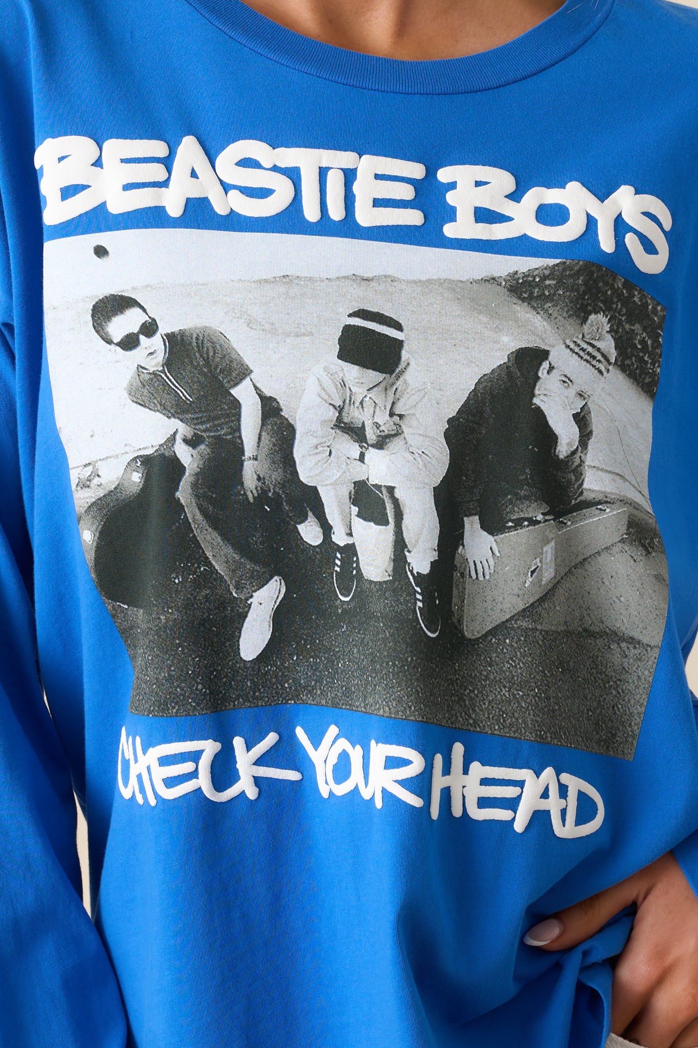 A close-up of the "Check Your Head" album art on the chest of the cobalt blue tee, emphasizing the intricate design and fabric texture.
