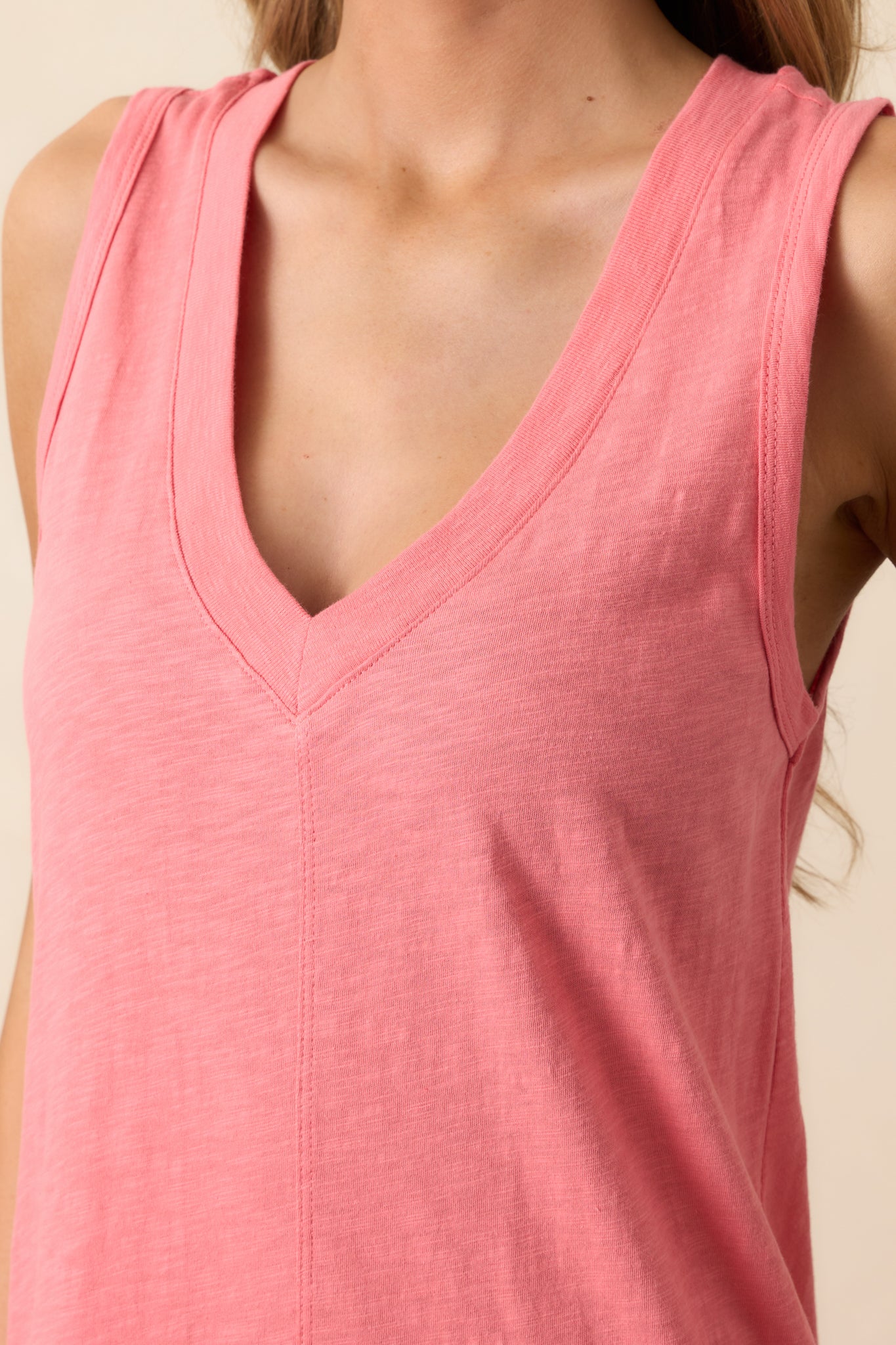 A close-up of the sunset pink dress highlighting the v-neckline and smooth, lightweight cotton fabric. The delicate stitching and airy design complement the stylish leg slits.