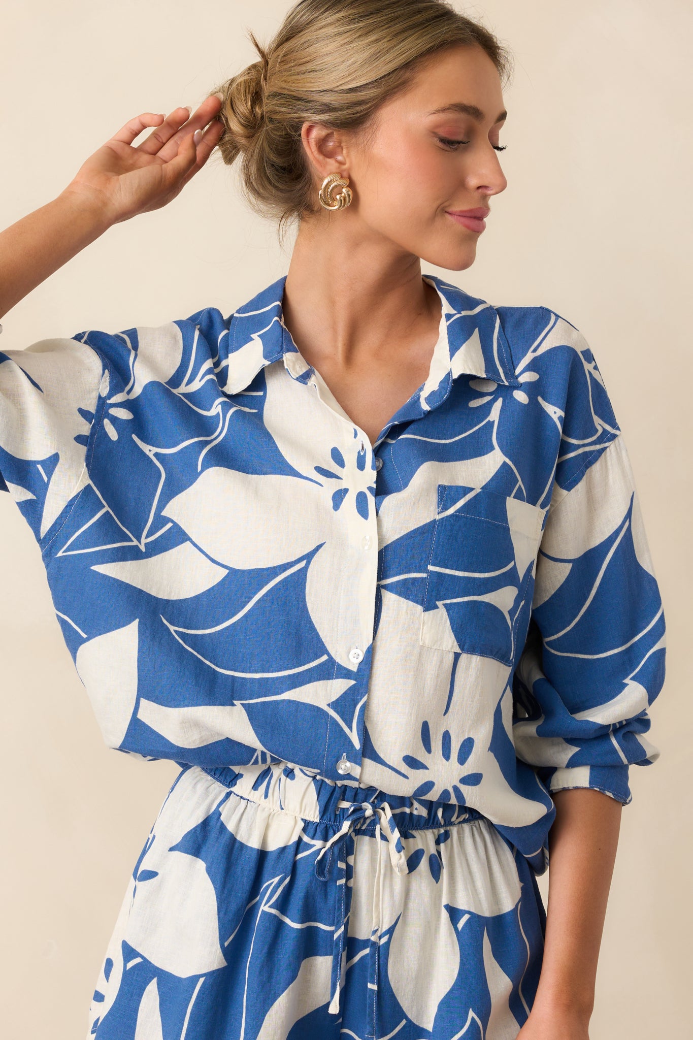 A zoomed-in view of the functional button front and long sleeves with button cuffs, showcasing the ivory and blue tropical print and lightweight fabric.