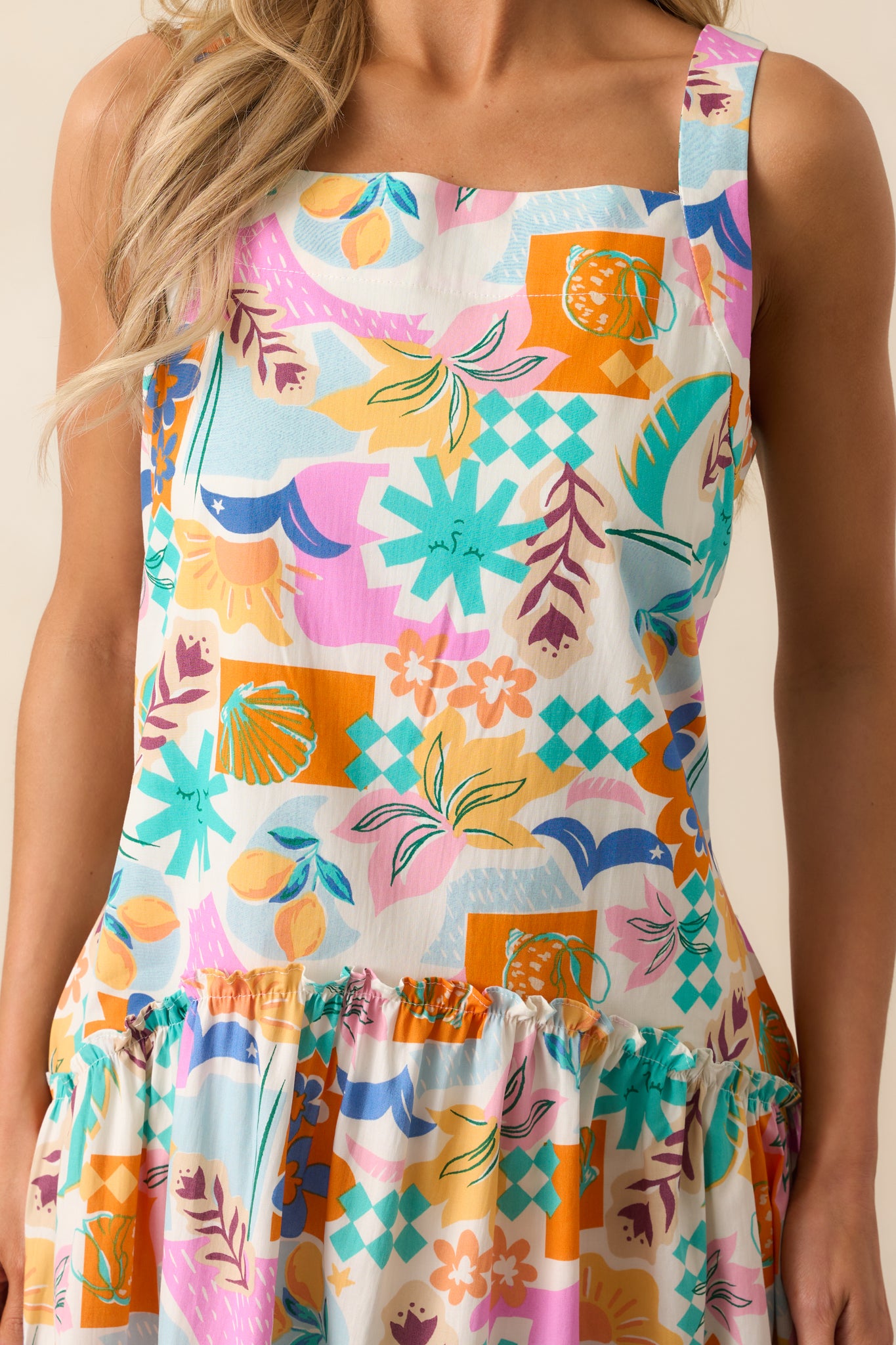 A close-up of the ruffle detailing and the textured fabric of this pink dress, highlighting the multicolor tropical print and the high square neckline.