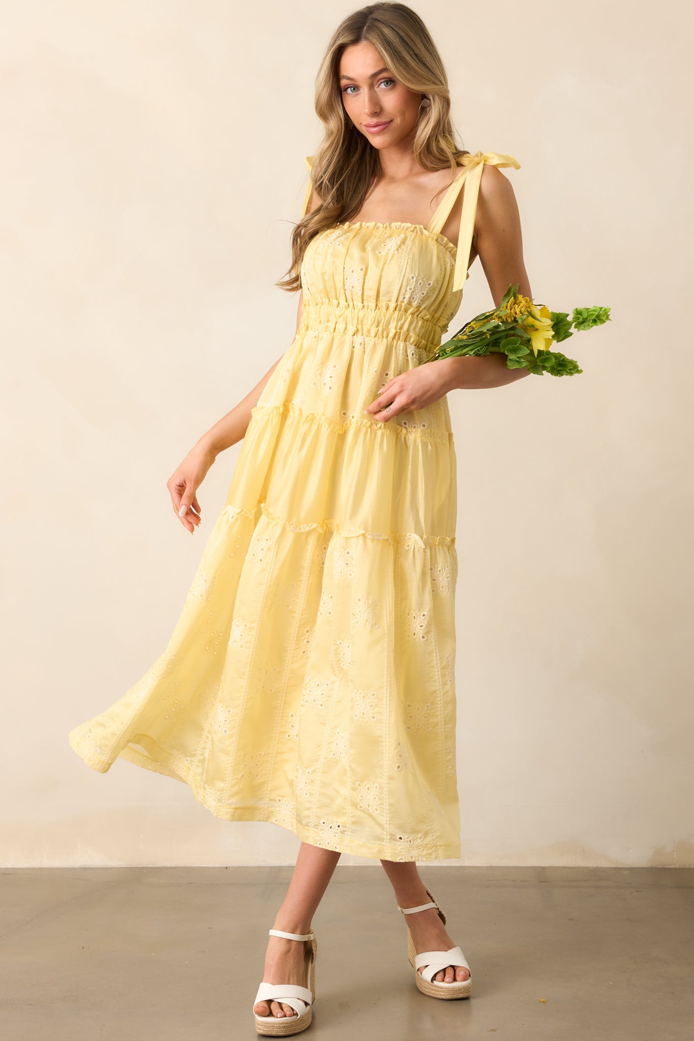 A delicate yellow midi dress with embroidered eyelet fabric, ruffle trim, and a graceful silhouette.
